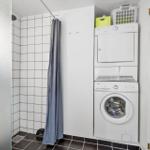 Shower with curtain and stacked washer-dryer unit against white wall.