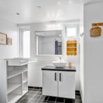 Bathroom with sink, mirror, and changing table. Black tiles and white walls.