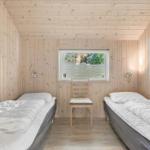 Two beds, chair, and window in a wood-paneled room.