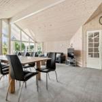 Large room with dining table, sofa, and TV. Wooden walls, large windows, and fireplace.