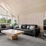 Living room with two black sofas, wooden table, and TV. Wooden walls and large windows.