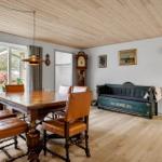 Esszimmer mit Holztisch, Lederstühlen und grüner Bank. Holzdecke und große Fenster.