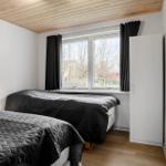 Zwei Betten mit dunklen Bezügen, Fenster mit schwarzen Vorhängen und Holzdecke.