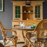 Rattan-Stuhl um einen Holztisch mit Kerze und Spielboxen. Hintergrund: Holzschrank und Wandbild.