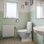 Badezimmer mit Toilette, Waschbecken und Fenster. Wandfliesen und Mosaikboden.