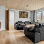 Wohnzimmer mit zwei schwarzen Ledersofas, Holzboden und Holzdecke. Fenster mit Vorhängen und Fernseher.