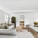 Wohnzimmer mit Sofa, Sessel und Holzboden. Durchgang zur Küche sichtbar.