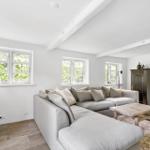 Wohnzimmer mit grauem Sofa, Holztisch und Fenstern mit Blick auf Grün.