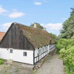 Ein traditionelles Haus mit Strohdach und Fachwerk, umgeben von Grünflächen und Bäumen.