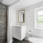 Badezimmer mit Dusche, Waschbecken und Toilette. Wände und Boden sind mit Stein verkleidet.