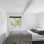 Schlafzimmer mit Bett, zwei Fenstern und weißen Wänden.