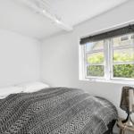 Schlafzimmer mit Bett, Fenster und Nachttisch mit Lampe.