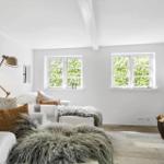 Wohnzimmer mit Sofa, Kamin und zwei Fenstern. Holzboden und weiße Wände.