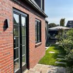 Rotes Backsteinhaus mit Gartenterrasse und Sonnenschirm. Pflasterweg und grüner Rasen.