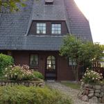 Haus mit dunkelrotem Ziegelmauerwerk, Schieferdach und Rosenbeeten im Vorgarten.