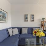 Ein Wohnzimmer mit blauem Sofa, Glas-Tisch und Wandbildern.