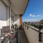 Balcony with chairs and table, overlooking rooftops and sky.