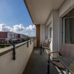 Terrasse mit Sitzgelegenheit und Blick auf Wohngebäude unter blauem Himmel.