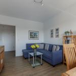 Wohnbereich mit blauem Sofa, Glas-Tisch und Holzmöbeln.