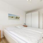 Schlafzimmer mit Doppelbett, Schrank und Nachttisch. Wandbild zeigt Dünenlandschaft.