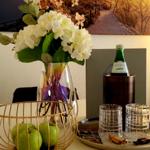 Tisch mit Blumen, Äpfeln, Gläsern und Mineralwasser im Hintergrund