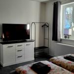 Zwei Betten, Fernseher und Kleiderständer im Schlafzimmer. Durchgang ins Wohnzimmer.