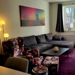 Wohnzimmer mit Sofa, Sessel und Teppich. Fenster und Tür mit Vorhängen.