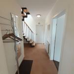 Hallway with coat rack, staircase, and doorways. Tile floor and white walls.