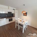 Kitchen with dining area, white furniture, wooden floor, and hanging lamp.