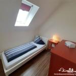 A bedroom with sloped ceilings, a bed, nightstand, and dresser.