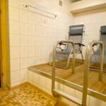 Sauna mit zwei Liegestühlen und Metallgeländern. Fliesenwand und Holzboden.