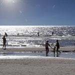 Sonniger Strand mit Menschen, die im Wasser spielen und entlang des Ufers gehen.
