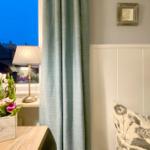 Schlafzimmer mit Bett, Vorhang und Blumen auf Nachttisch.