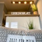 Ein Kissen mit Aufnäher steht vor einer Küchenzeile mit Schriftzug und Pflanzen.