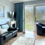 Wohnzimmer mit Sofa, Sessel und Balkonblick. Fernseher und Wandbild sind vorhanden.