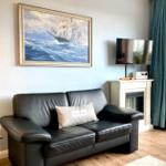 Schwarzes Ledersofa mit Kissen, Wandbild, Fernseher und Kamin im Wohnzimmer.