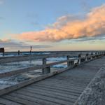 Holzbrücke führt zum Strand von Zingst. Im Hintergrund sind Wellen und Wolken zu sehen.