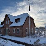 Rotes Backsteinhaus mit schneebedecktem Dach und Flagge im Vorgarten.