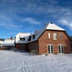 Rotes Backsteingebäude mit schneebedecktem Dach und weißen Fenstern.