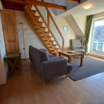 Wohnzimmer mit Sofa, Tisch und Holztreppe. Große Fenster und Holzboden.