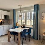 Kitchen with dining table, windows, and curtains. Living area with table and lamps.