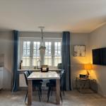 Dining area with table, chairs, and window. Kitchen and TV wall are visible.