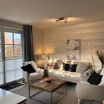 Living room with sofa, two chairs, and wooden table. Doorway to outdoor area.