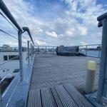 Roof terrace with wooden floor and metal railing. Buildings and sky with clouds are visible in the background.