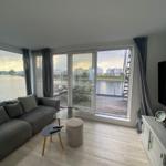 Living room with view of water and terrace with table and chairs.