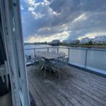 Terrace with table and chairs by water, overlooking houses and cloudy sky.