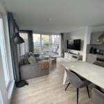 Living and dining area with sofa, TV, and view of balcony.