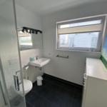Bathroom with shower, sink, and toilet. Window with blinds.