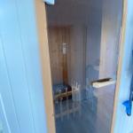 Sauna with wooden walls and glass door. Wooden bench and heater visible.