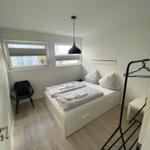 Bedroom with double bed, clothes rack, and two windows with blinds.